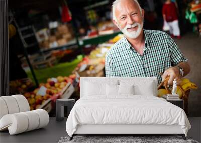 Handsome senior man shopping for fresh fruit and vegetable in a market Wall mural