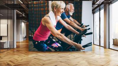 Happy fit mature woman and man cycling on exercise bikes to stay healthy Wall mural