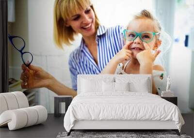 Happy mother with her cute daughter choosing glasses in optics store Wall mural