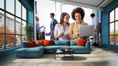 Happy multiethnic business women working together online on a laptop in corporate office. Wall mural