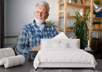 Happy senior man reading book at home Wall mural