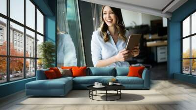 Happy woman manager holding tablet and standing in modern office Wall mural