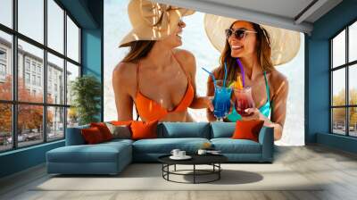 Happy women wearing bikinis and drinking cocktails on a tropical beach during summer vacation Wall mural