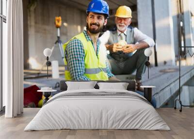 Happy young and senior engineer worker sitting at building site on break Wall mural