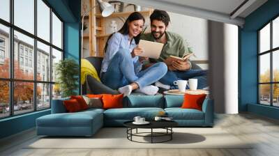 Happy young couple relaxing. Reading something on book and tablet computer. Wall mural