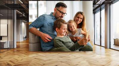 Happy young family having fun time at home. Parents with children using digital device. Wall mural