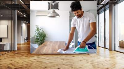 Happy young handsome black man ironing clothes at home Wall mural