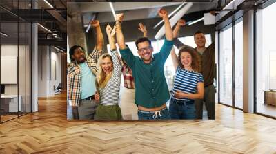 Happy young successful business team celebrating a triumph with arms up in startup office. Wall mural