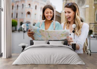 Holidays, travel, friends and tourism concept. Beautiful girls looking into tourist map in the city Wall mural