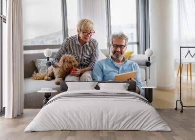 Lovely smiling mature couple having fun while using tablet at home Wall mural