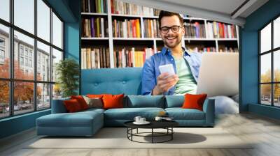 Man in library talking on cell phone and working on laptop Wall mural