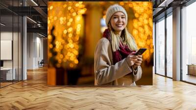 Portrait of beautiful young woman using her mobile phone in the street with christmas decoration. Wall mural