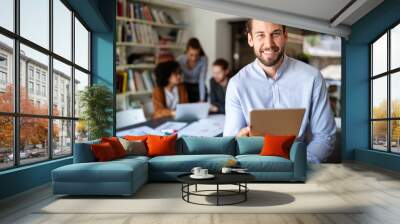 Portrait of businessman holding tablet in office and colleagues discussing in background Wall mural