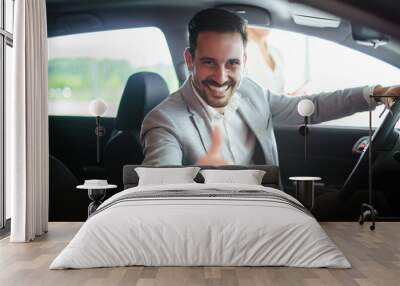 Portrait of handsome young man taking luxury car for test drive, sitting inside and smiling Wall mural