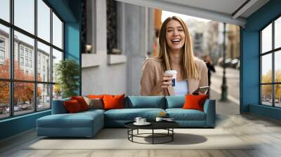 Portrait of happy business woman with coffee and mobile phone on her way to work on city street. Wall mural