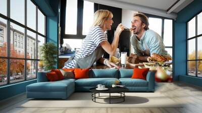 Portrait of happy young couple cooking together in the kitchen at home. Wall mural