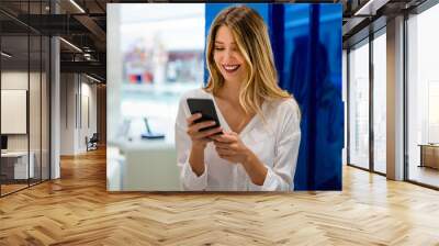 Portrait of happy young woman buying a new smartphone in store. Shopping a new digital device Wall mural