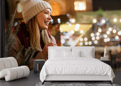 Portrait of happy young woman eating donuts on the christmas market. Holiday fun people concept Wall mural