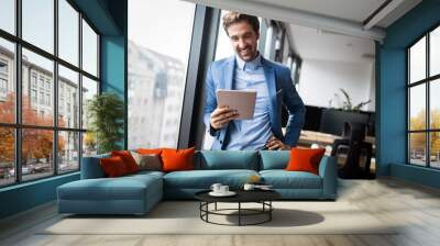 Portrait of young businessman smiling while using digital tablet in office Wall mural