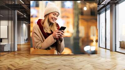 Portrait of young smiling beautiful woman using smartphone on the street at winter Wall mural