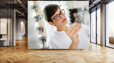 pretty young woman is choosing new glasses at optics store Wall mural