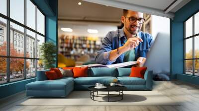 Smiling male student working and studying in a library Wall mural