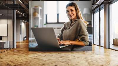 Smiling pretty woman using laptop for work freelance social media or relaxation. Wall mural