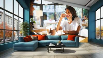 Smiling young african couple sitting at a table at a cafe drinking coffee and talking together Wall mural