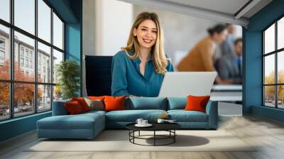 Successful young attractive businesswoman working on laptop in her workstation at office Wall mural