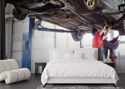 Two mechanics in uniform are working in auto service with lifted vehicle Wall mural