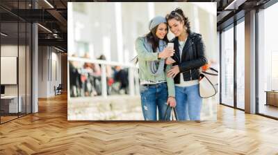 Two young women looking at the phone while being close to eatch Wall mural