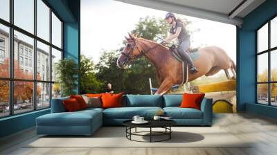 Young female jockey on horse leaping over hurdle Wall mural