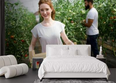 Young happy couple farming vegetables in greenhouse Wall mural