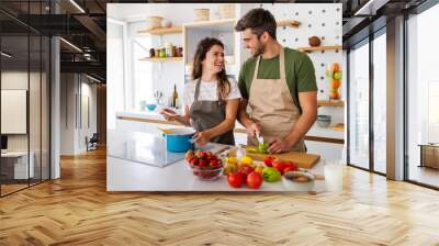 Young happy couple is enjoying and preparing healthy meal in their kitchen Wall mural