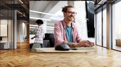 Young hipster man smiling while working on computer desk in office Wall mural