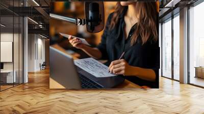 A woman sits at a desk with a microphone, laptop and papers. She is recording a podcast or radio show. Wall mural