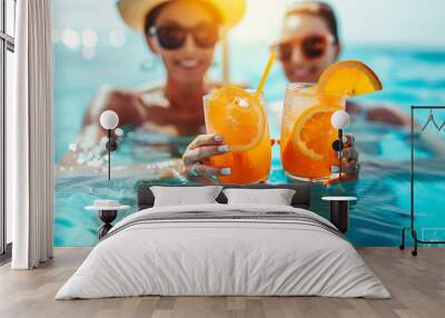 Two young women on vacation holding orange cocktails while sitting in a pool Wall mural