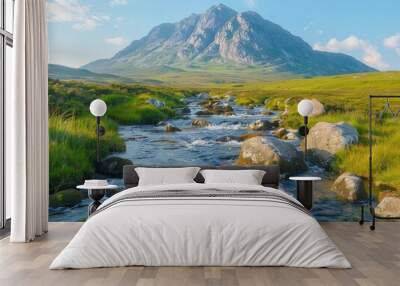 A serene mountain landscape with a flowing stream, lush grass, and a clear blue sky. Wall mural