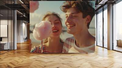 A young man and woman enjoy cotton candy together outdoors, with a beach background. Wall mural