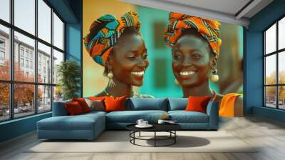 Two women in vibrant, traditional African attire share a joyful greeting. Their colorful headwraps and jewelry enhance the cheerful, warm atmosphere. Wall mural