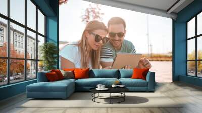 Beautiful girl and her boyfriend, wearing sunglasses and browsing internet on tablet Wall mural