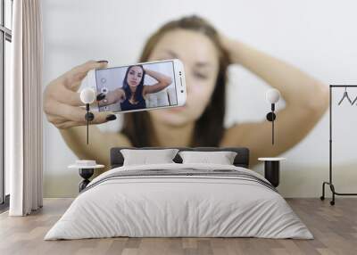 Beautiful young woman photographing herself with phone at home Wall mural