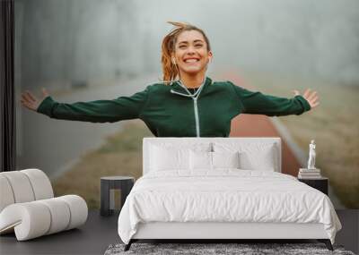 Close photo of young excited woman runner with beautiful smile and outstretching arms running towards camera on foggy morning. Wall mural