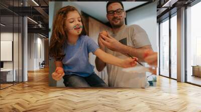 Cute little girl painting easter eggs, mommy and daddy are helping. Her face is messed with paint, she is happy and content. Wall mural