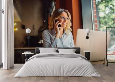 portrait of young business woman with glasses sitting in cafe in front of her laptop and talking on  Wall mural