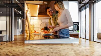 Romantic couple is cooking on kitchen. Young couple spending time in kitchen, making a pasta. Wall mural