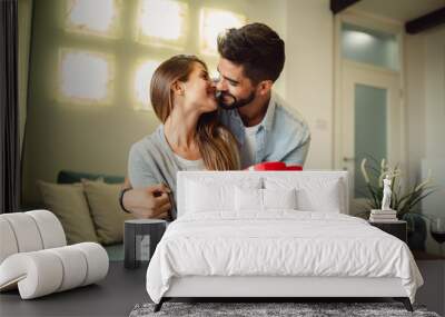 Young woman receiving a surprise gift box from her boyfriend at home. Wall mural