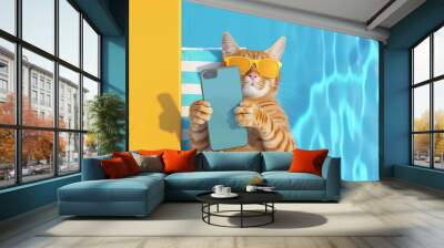 A cat wearing sunglasses holds a phone next to a pool on a sunny day Wall mural