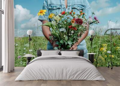 A person wearing a denim jacket holds a large bouquet of colorful wildflowers in a sunny meadow Wall mural