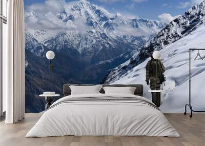 A Indian army soldier in uniform with guns walks in the snow-covered mountains Wall mural